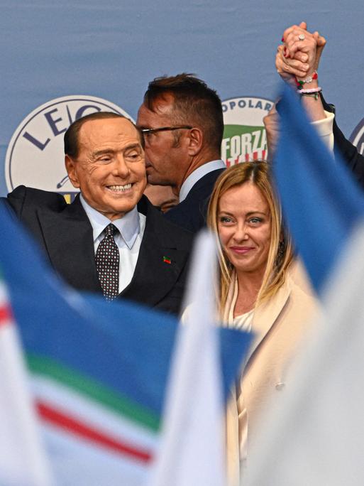 Von links: Chef der Lega Partei Matteo Salvini, Forza Chef Silvio Berlusconi und Giorgia Meloni zusammen auf einer Wahlbühne am 22. September in Rom, Italien. Vor ihnen wehen Fahnen.