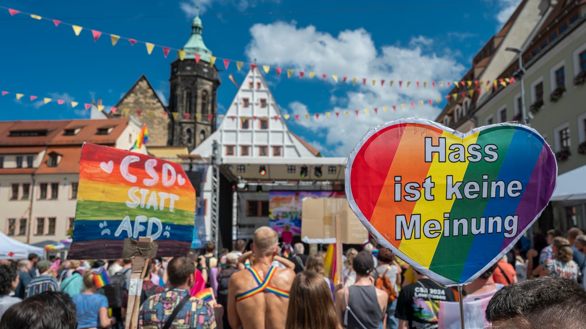 Zahlreiche Teilnehmer versammeln sich während des Christopher Street Day in Pirna auf dem Markt. Im Hintergrund die Stadtkulisse, davor Menschen mit allerlei Regenbogenfarben. Und Transparenten die sagen "CSD statt AFD" und "Hass ist keine Meinung".