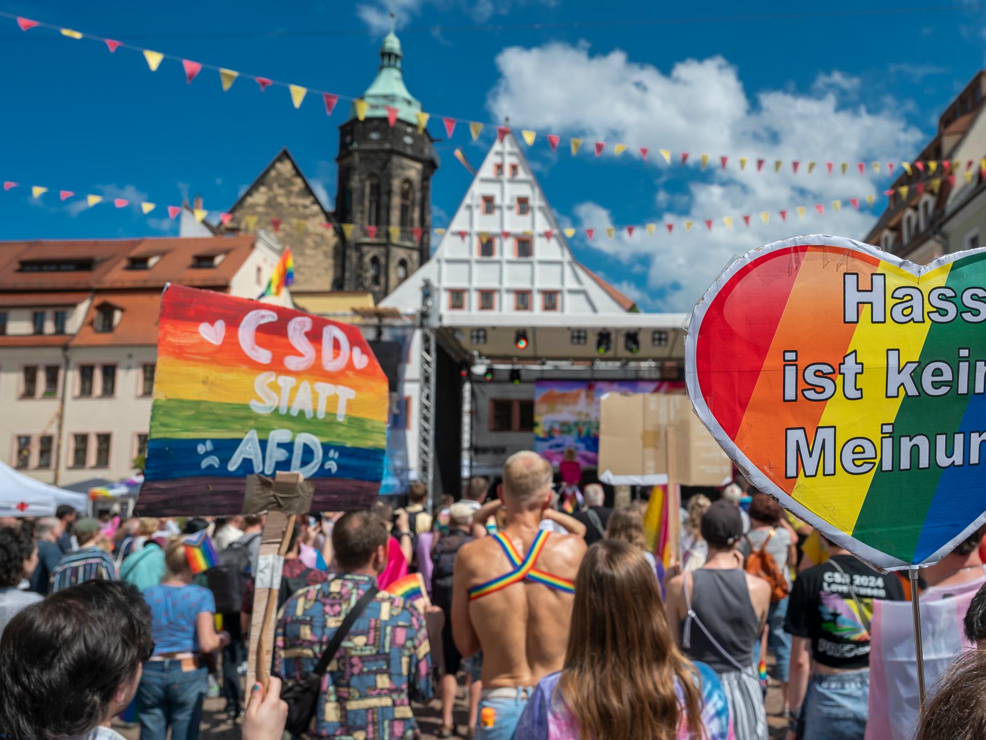 Zahlreiche Teilnehmer versammeln sich während des Christopher Street Day in Pirna auf dem Markt. Im Hintergrund die Stadtkulisse, davor Menschen mit allerlei Regenbogenfarben. Und Transparenten die sagen "CSD statt AFD" und "Hass ist keine Meinung".