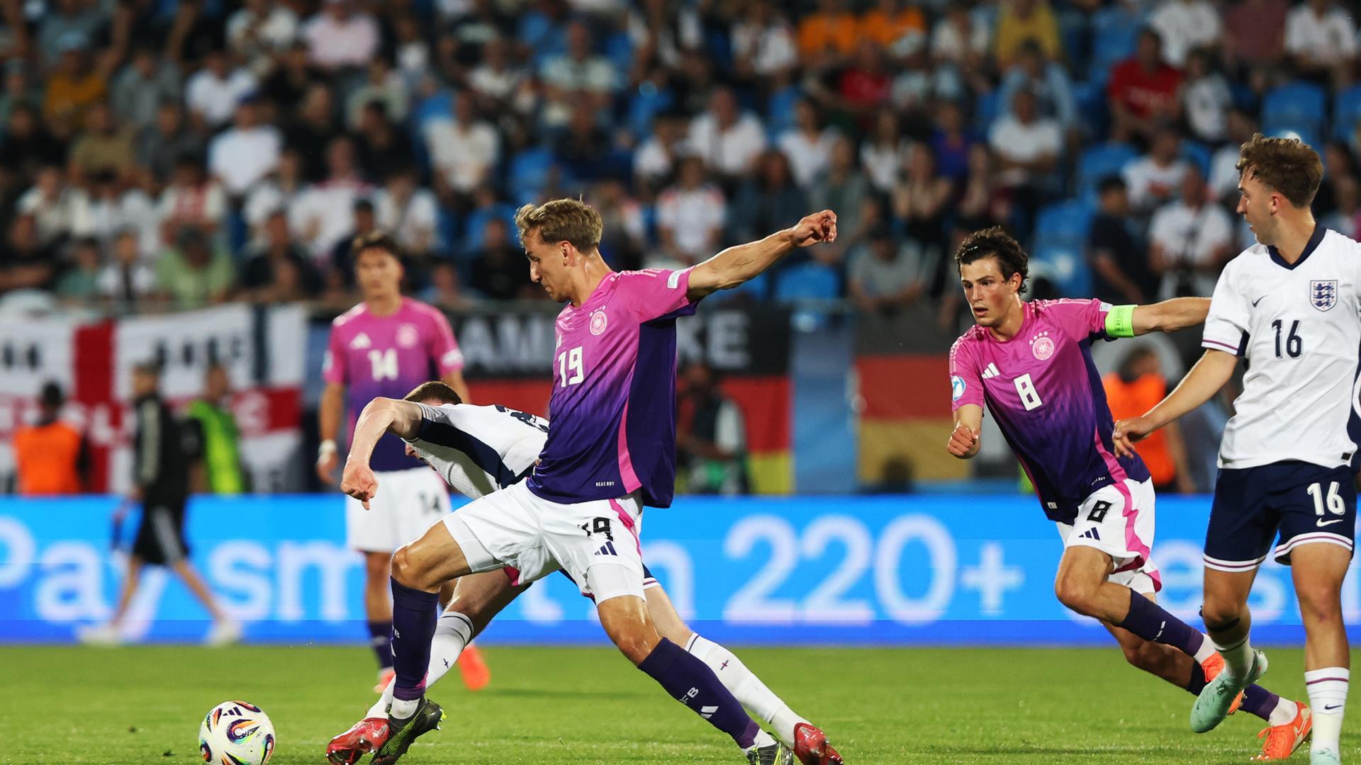 Drei deutsche Fußballer in pinken Trikots und zwei englische Fußballer in weißen Trikots kämpfen um den Ball. Drei deutsche Fußballer in pinken Trikots und zwei englische Fußballer in weißen Trikots kämpfen um den Ball.