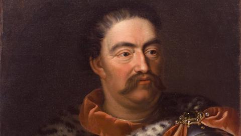 Eine alte Malerei. Darauf ist der polnische König Jan Sobieski zu sehen. Er trägt einen Schnauzbart und eine mit Tüchern verzierte Rüstung.