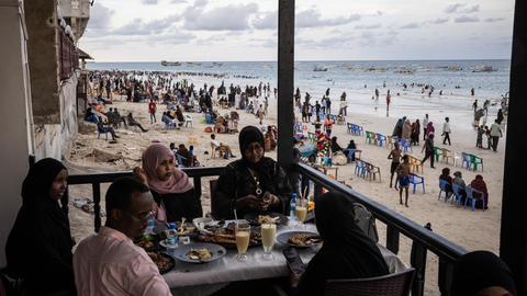 Gäste sitzen in einem Restaurant am Lido Beach von Mogadischu in Somalia, während im Hintergrund am Strand sehr viele Menschen ihre Freizeit verbringen.