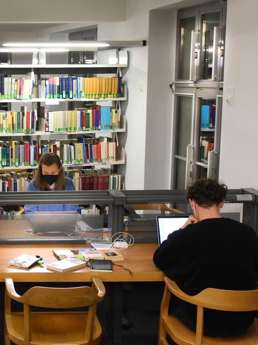 In der Universitätsbibliothek sitzen Studenten an mit Computern bestückten Tischen. 
