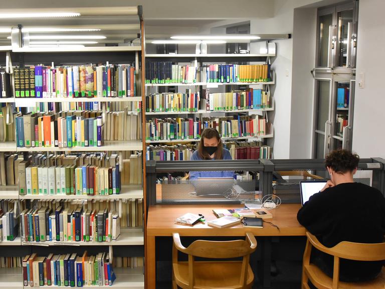 In der Universitätsbibliothek sitzen Studenten an mit Computern bestückten Tischen. 