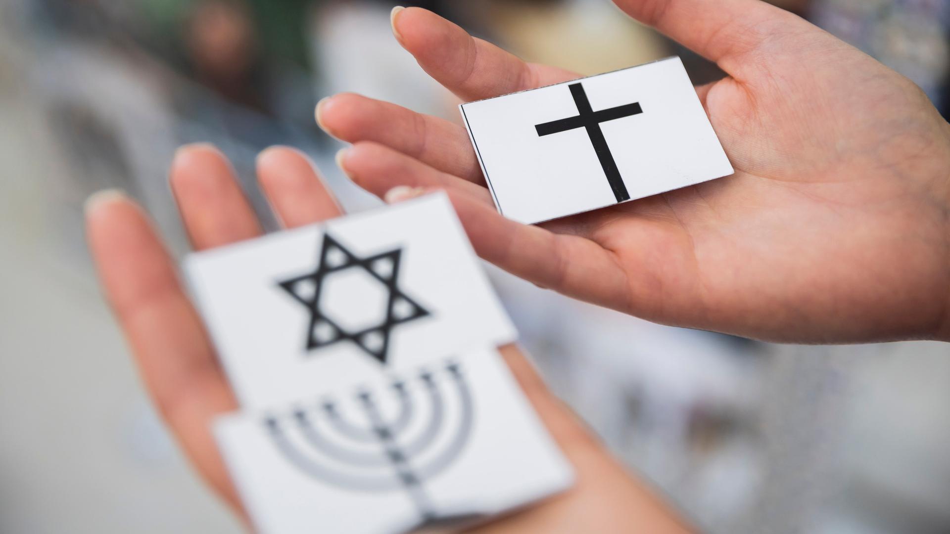 Eine Frau hält drei Karten, eine mit dem Kreuz des Christentums und dem Davidstern sowie der Menora des Judentums.