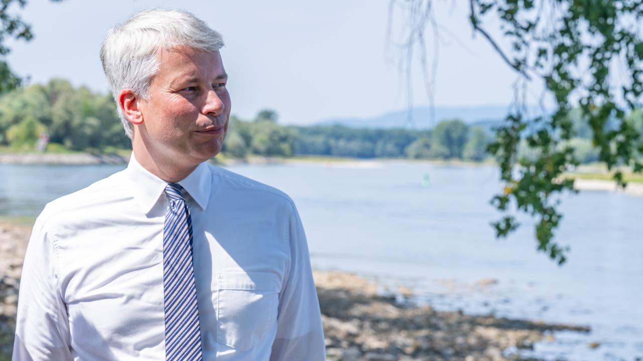 Der neue Bundesverkehrsminister Steffen Bilger blickt auf die Donau und informiert sich über den Ausbau zwischen Straubing und Vilshofen. Er trägt ein weißes Hemd und Krawatte. 