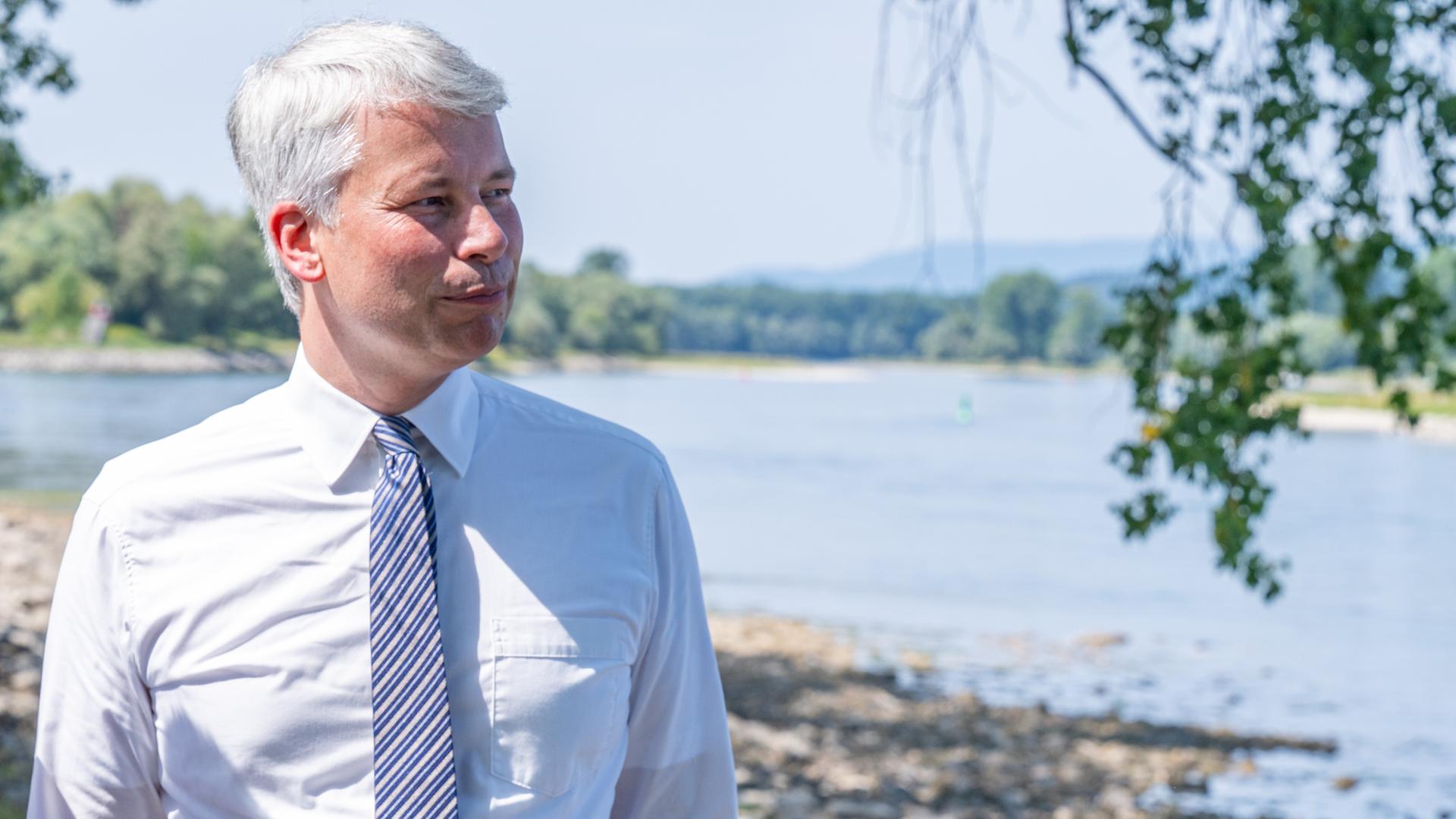Der neue Bundesverkehrsminister Steffen Bilger blickt auf die Donau und informiert sich über den Ausbau zwischen Straubing und Vilshofen. Er trägt ein weißes Hemd und Krawatte. 