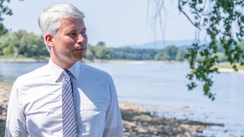 Der neue Bundesverkehrsminister Steffen Bilger blickt auf die Donau und informiert sich über den Ausbau zwischen Straubing und Vilshofen. Er trägt ein weißes Hemd und Krawatte. 