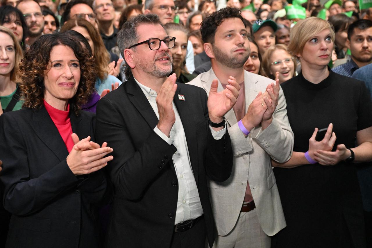 Bettina Jarasch, Werner Graf und Felix Banaszak stehen in einer Menschenmenge und klatschen.