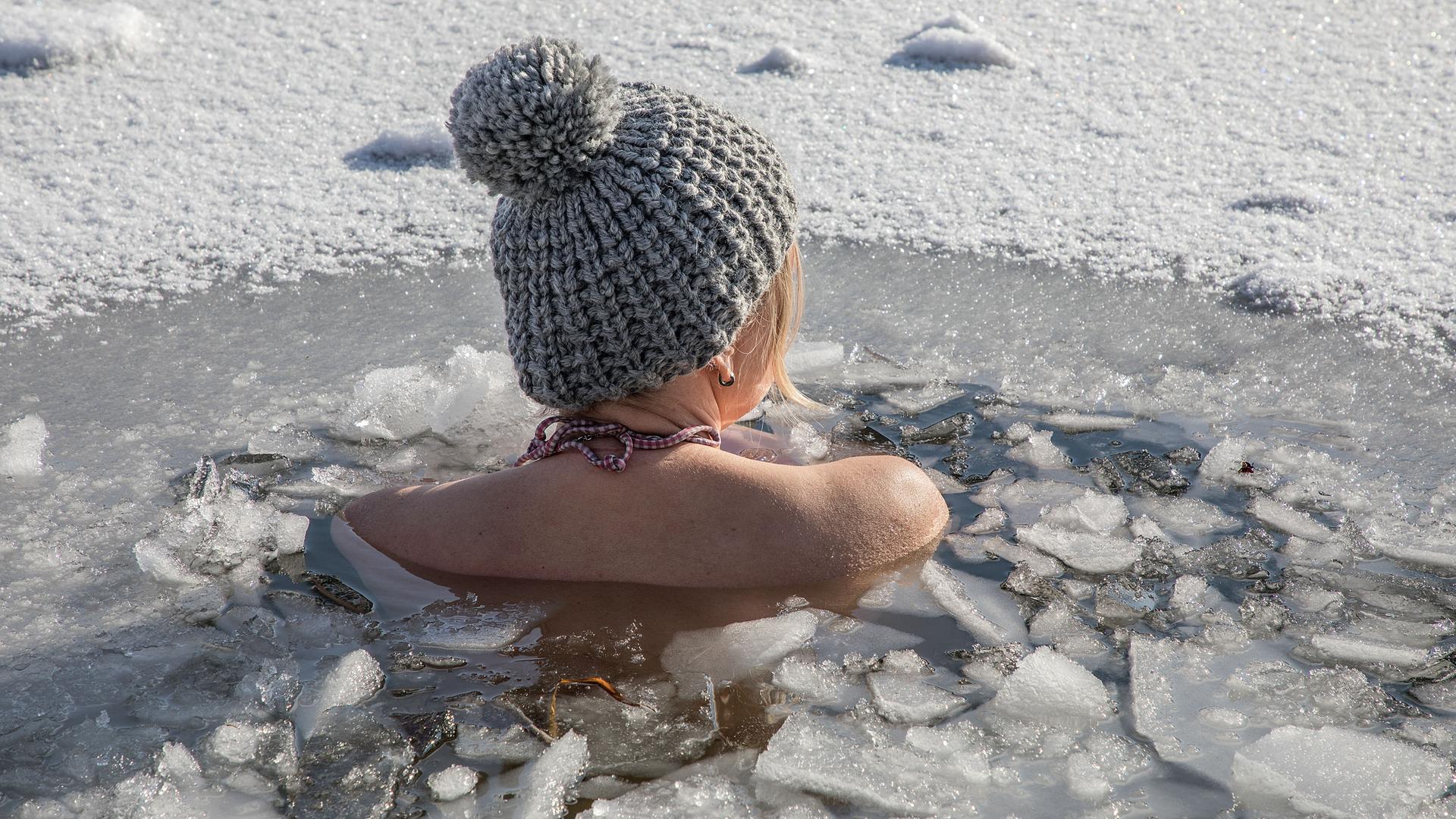 Eine Frau beim Eisbaden bei einer gefrorenen Wasserfläche im Winter, 2021.