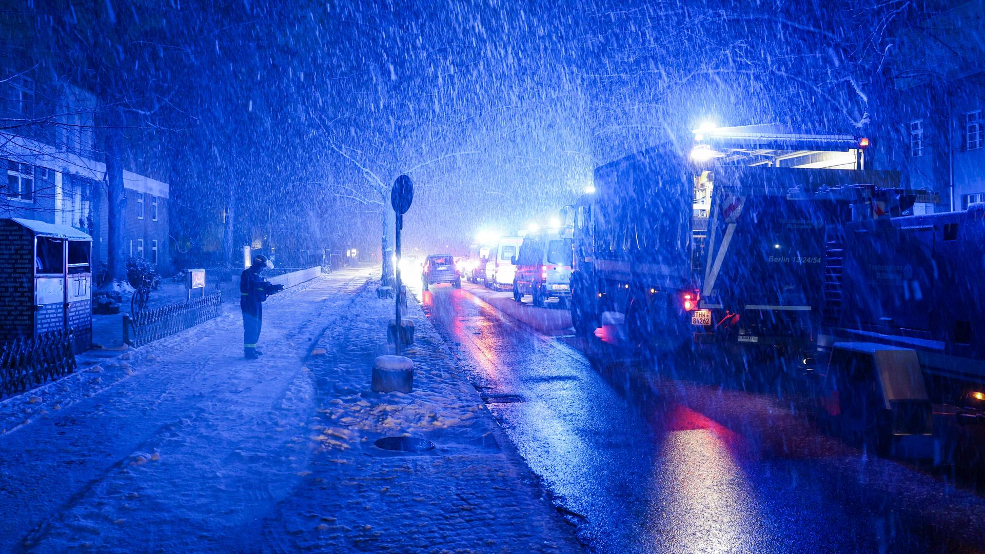 Eine uniformierte Person steht neben einem THW-Fahrzeug auf der Straße. Es schneit stark, die umliegenden Gebäude sind dunkel.