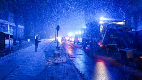 Eine uniformierte Person steht neben einem THW-Fahrzeug auf der Straße. Es schneit stark, die umliegenden Gebäude sind dunkel.