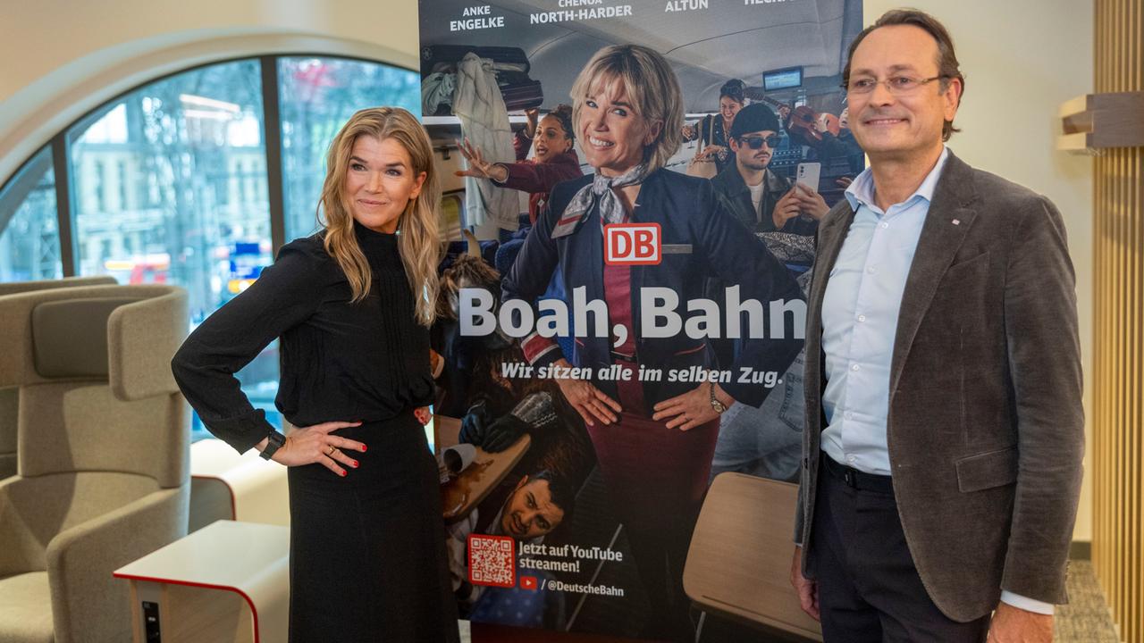 Entertainerin Anke Engelke und Michael Peterson, DB Vorstand Personenfernverkehr, vor dem Plakat zur Kampagne "Boah, Bahn". Sie lächeln.