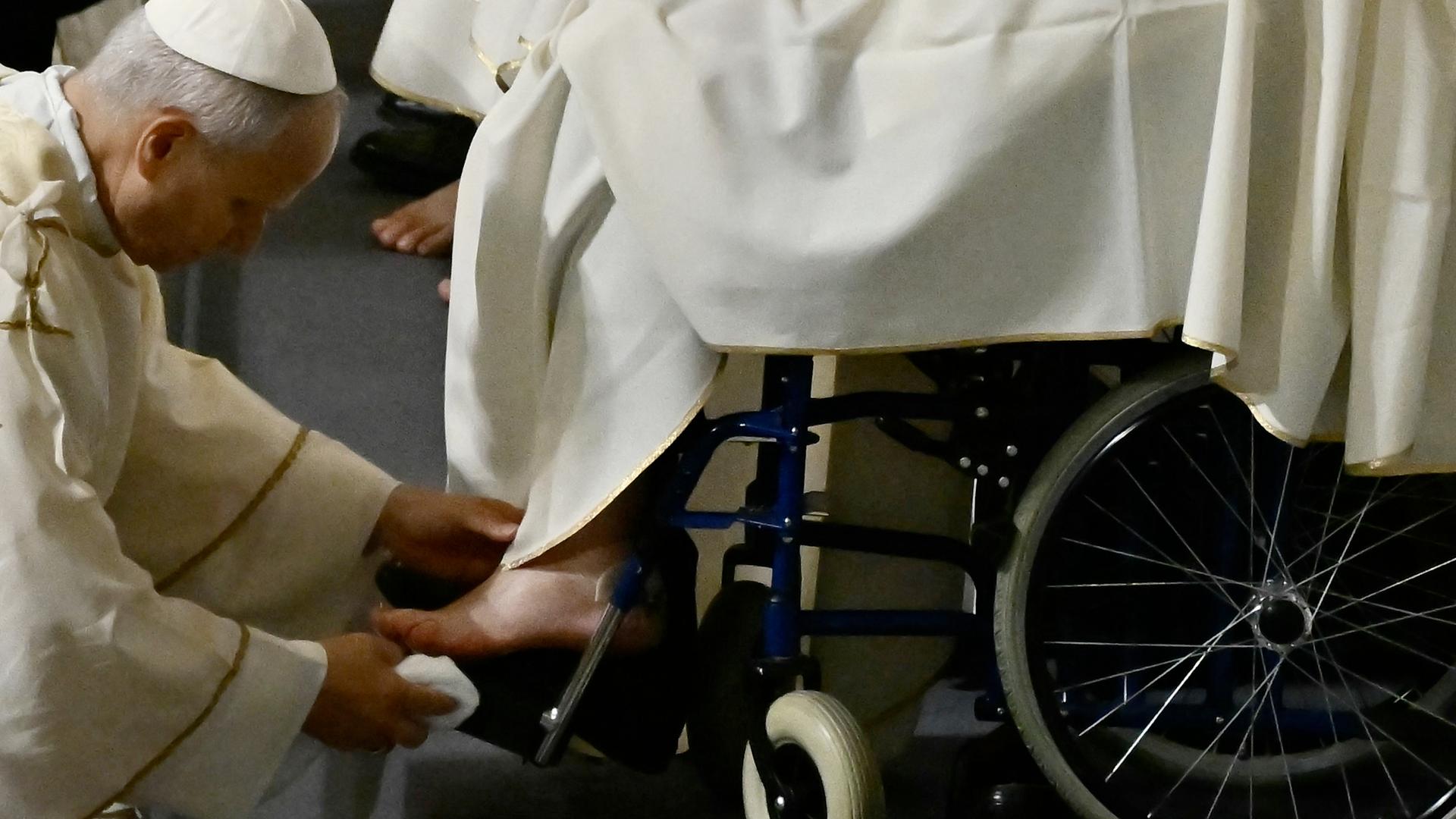 Papst Leo XIV. beugt sich vor und tupft einen nackt Fuß mit einem Tuch ab. Er trägt ein weißes Gewand.