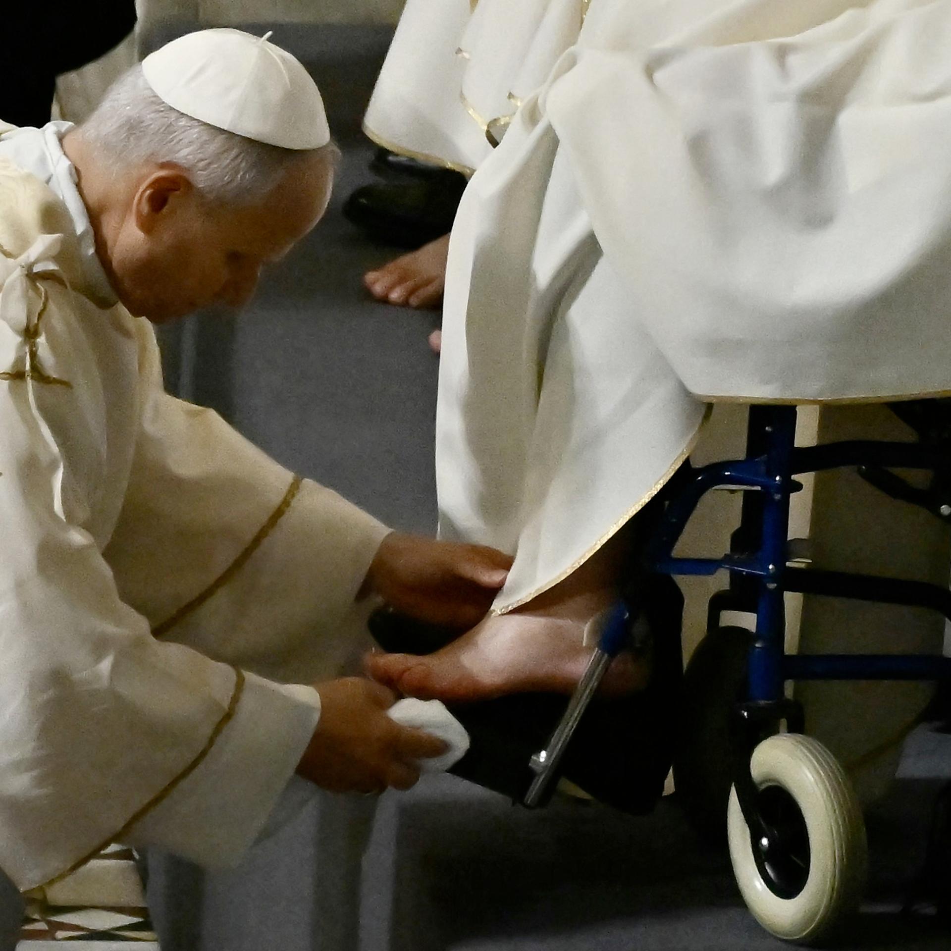 Papst Leo XIV. beugt sich vor und tupft einen nackt Fuß mit einem Tuch ab. Er trägt ein weißes Gewand.