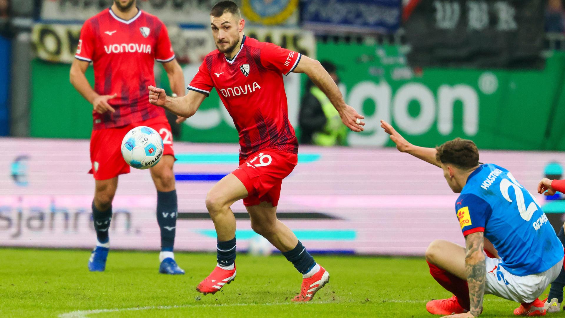 Ein Fußballspieler im roten Trikot umläuft einen Spieler im blauen Trikot.