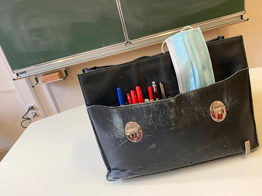 Die Tasche eines Lehrers steht auf dem Pult vor einer Tafel. 