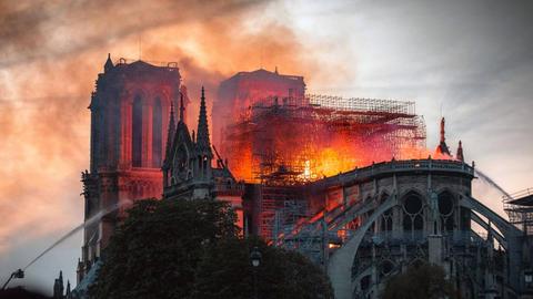 Eine Aufnahme aus dem Film "Notre-Dame in Flammen". Die bekannte Pariser Kirche brennt, die Flammen schlagen durch den Dachstuhl, am Rand wird versucht, mit Wasser zu löschen.