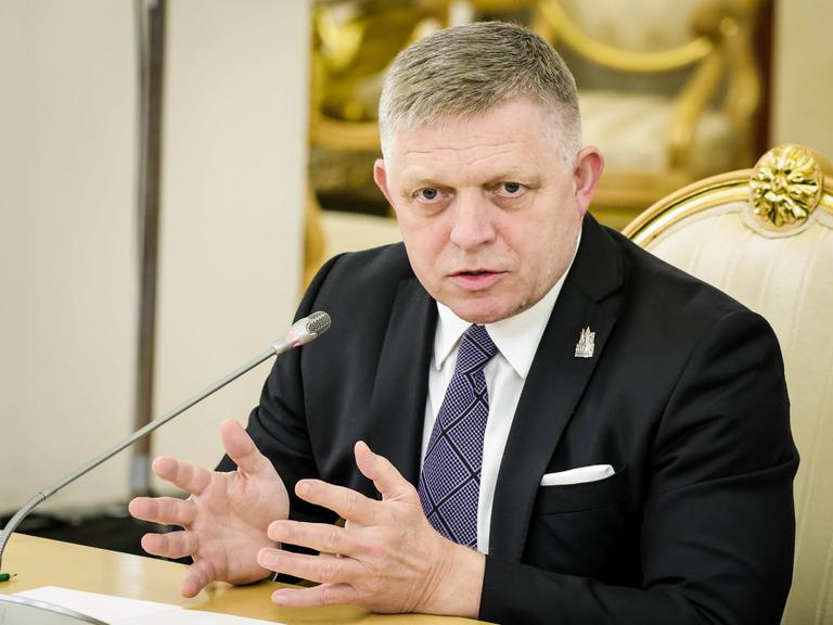 Der Slowakische Premier Fico sitzt vor einem Mikrofon an einem Tisch und gestikuliert.