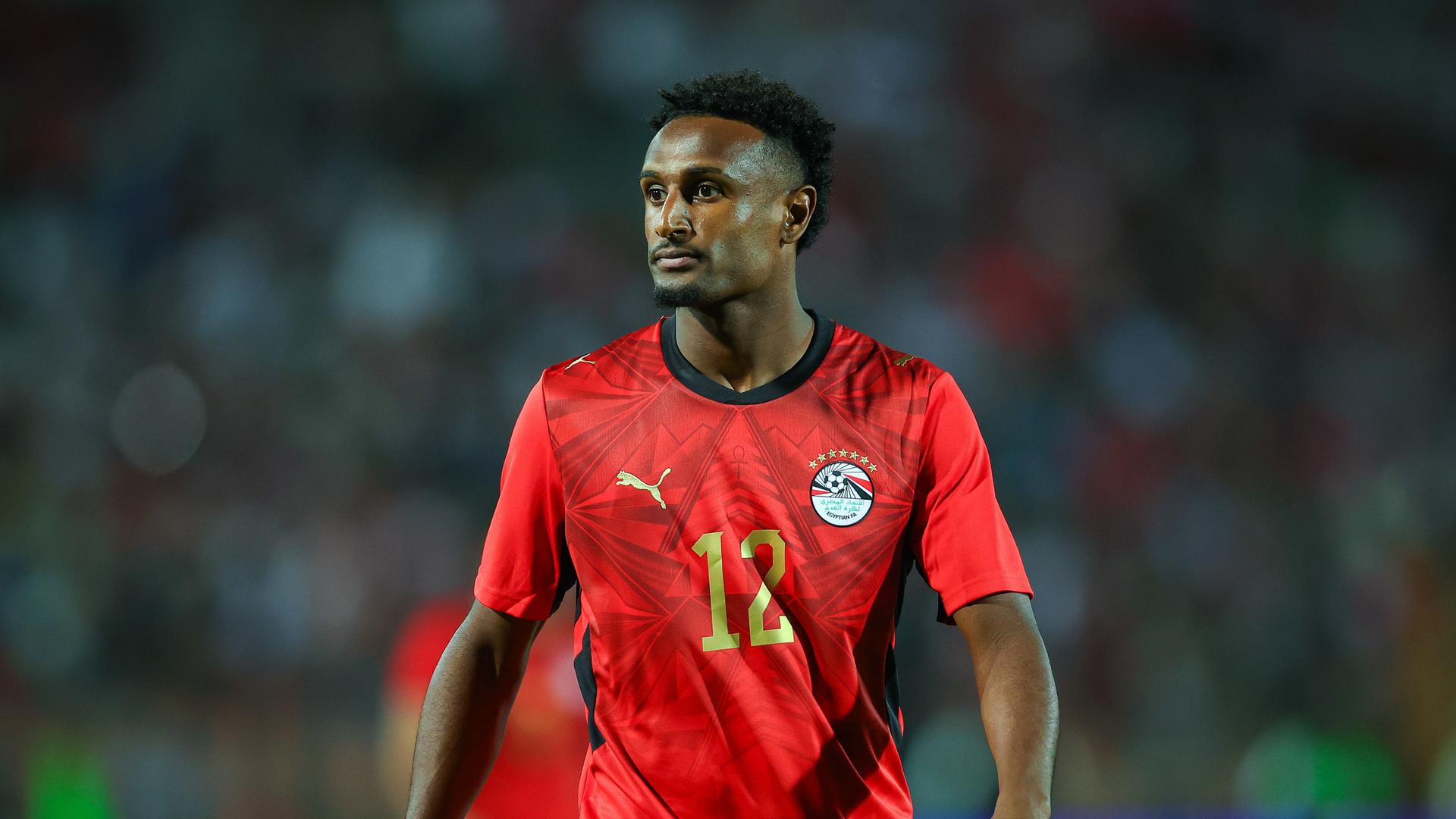 Ägyptens Fußball-Nationalspieler Haissem Hassan im roten Nationaltrikot. Das Trikot zeigt ein Emblem mit sieben Sternen und die Nummer 12 in goldener Farbe. Ägyptens Fußball-Nationalspieler Haissem Hassan im roten Nationaltrikot. Das Trikot zeigt ein Emblem mit sieben Sternen und die Nummer 12 in goldener Farbe.