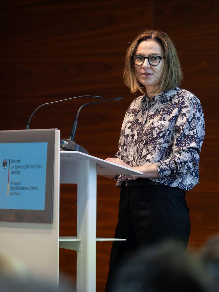 Małgorzata Ławrowska von Thadden steht bei einer Veranstaltung an einem Podium und spricht zu Publikum.