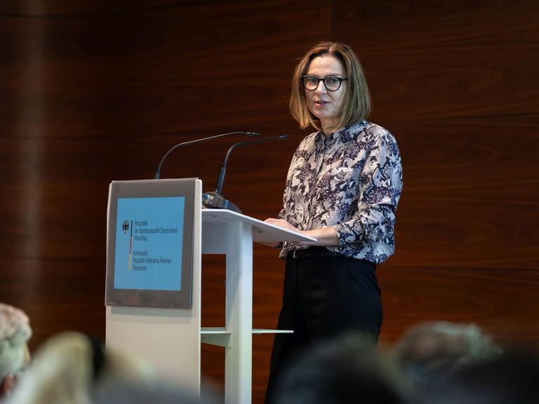 Małgorzata Ławrowska von Thadden steht bei einer Veranstaltung an einem Podium und spricht zu Publikum.