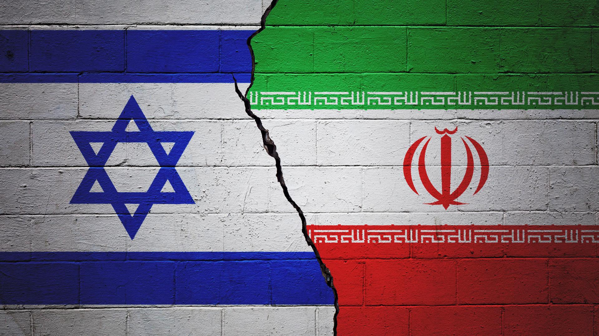 Eine rissige Ziegelwand, auf der links eine israelische und rechts eine iranische Flagge gezeichnet ist.