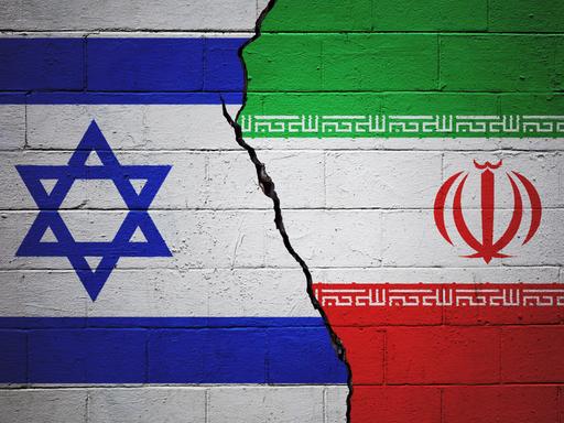 Eine rissige Ziegelwand, auf der links eine israelische und rechts eine iranische Flagge gezeichnet ist.