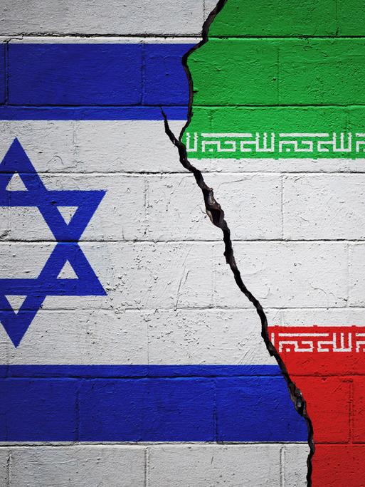 Eine rissige Ziegelwand, auf der links eine israelische und rechts eine iranische Flagge gezeichnet ist.