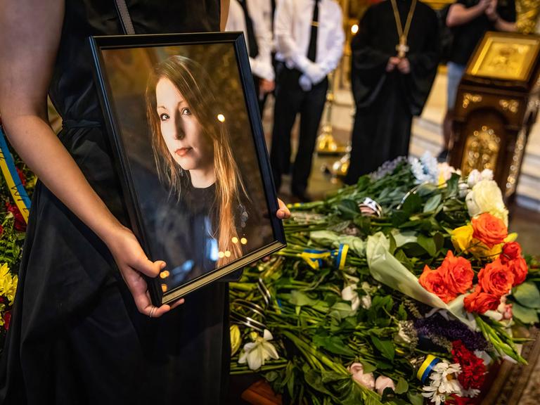 Ein Foto der ukrainischen Schriftstellerin Victoria Amelina wird von einer Person gehalten. Im Hintergrund sind Blumen zu sehen.