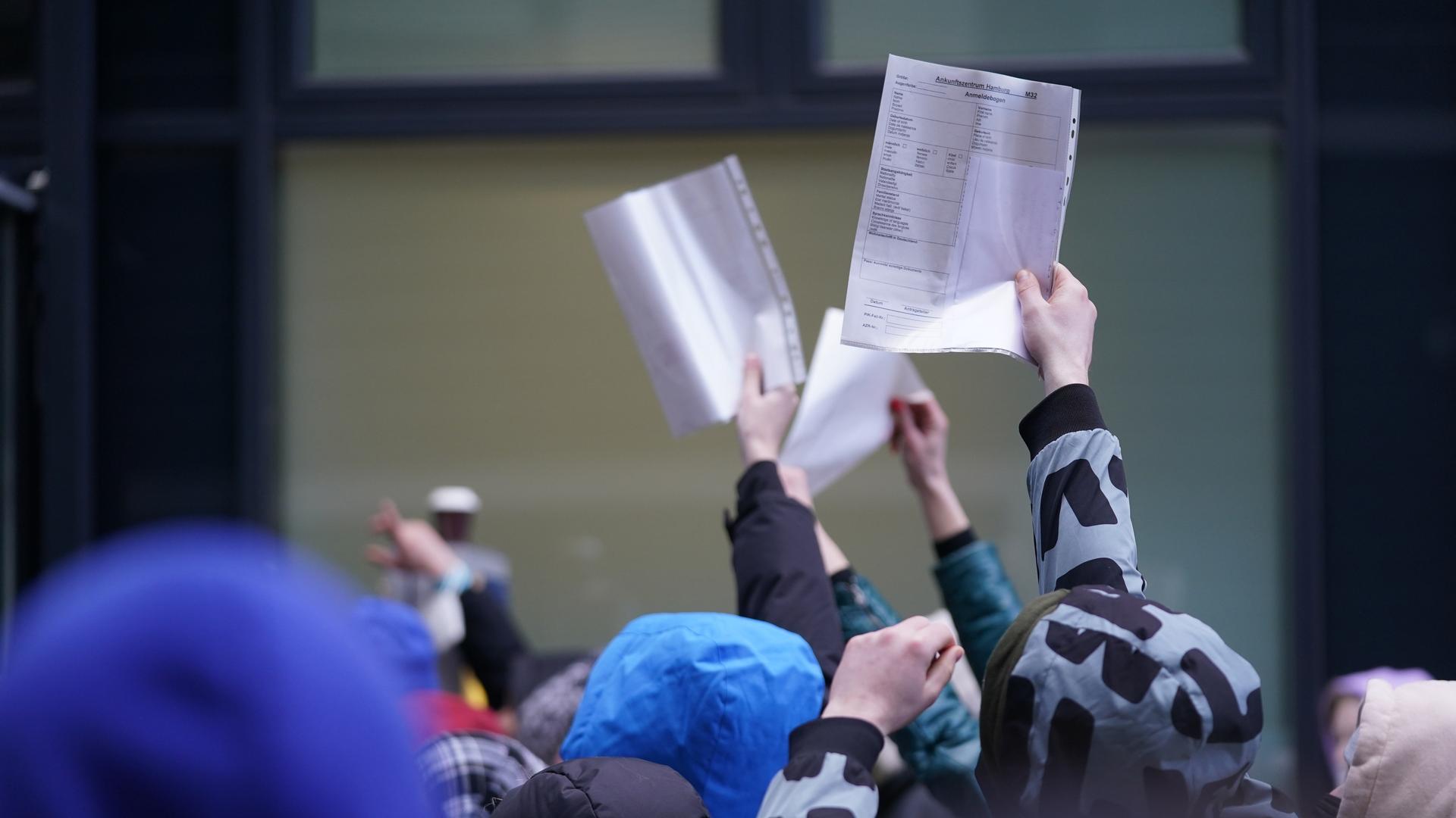 Menschen mit Formularen in der Hand in einer Warteschlange von einer Zentralen Ausländerbehörde.