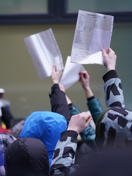Menschen mit Formularen in der Hand in einer Warteschlange von einer Zentralen Ausländerbehörde.