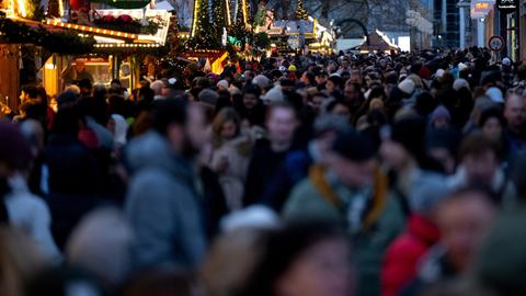 Zahlreiche Menschen gehen am Nachmittag in der Münchner Innenstadt durch die Fußgängerzone, in der Stände von einem Weihnachtsmarkt stehen.