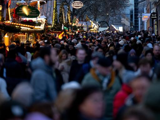 Zahlreiche Menschen gehen am Nachmittag in der Münchner Innenstadt durch die Fußgängerzone, in der Stände von einem Weihnachtsmarkt stehen.