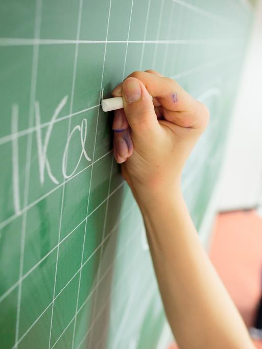 Die Hand eines Schülers schreibt etwas an eine Tafel Die Hand eines Schülers schreibt etwas an eine Tafel