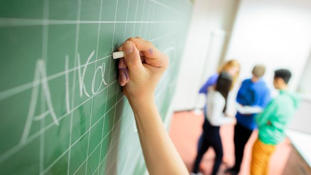 Die Hand eines Schülers schreibt etwas an eine Tafel
