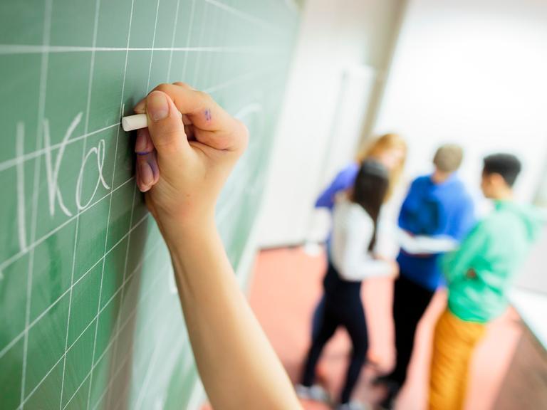 Die Hand eines Schülers schreibt etwas an eine Tafel Die Hand eines Schülers schreibt etwas an eine Tafel