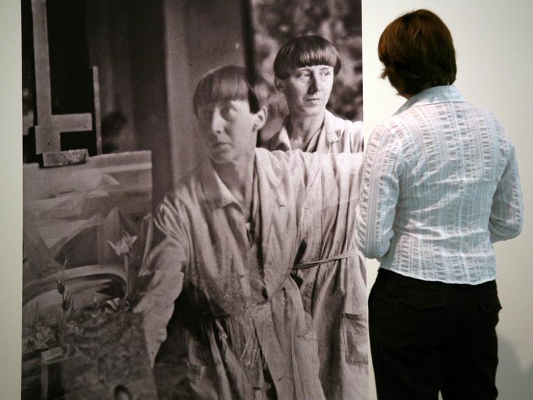 Eine Doppelbelichtung der Dada-Künstlerin Hannah Höch (Fotografie um 1930) betrachtet eine Besucherin in einer Ausstellung ihrer Werke. 