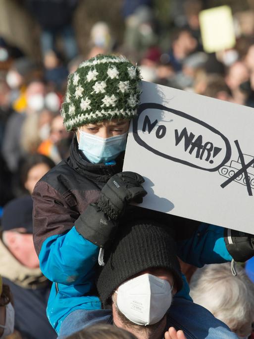 Ein Kind, getragen von einem Mann, hält ein Schild mit der Aufschrift "No War" in der Hand