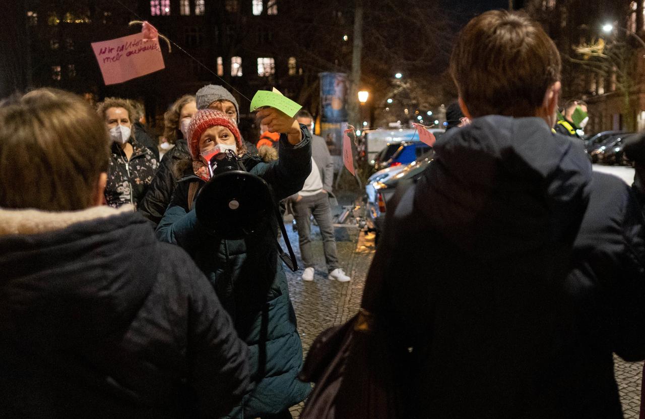 Eine Gruppe von Demonstranten mit Mundschutz, in der Mitte steht einem Frau mit einer Wollmütz, die in ein Megafon spricht.