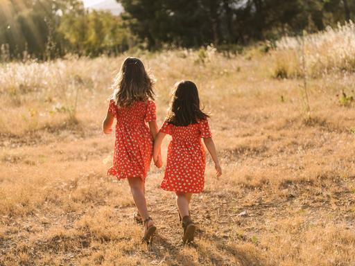 Zwei Schwester, die das gleiche Kleid tragen, gehen Hand in Hand durch die Natur.