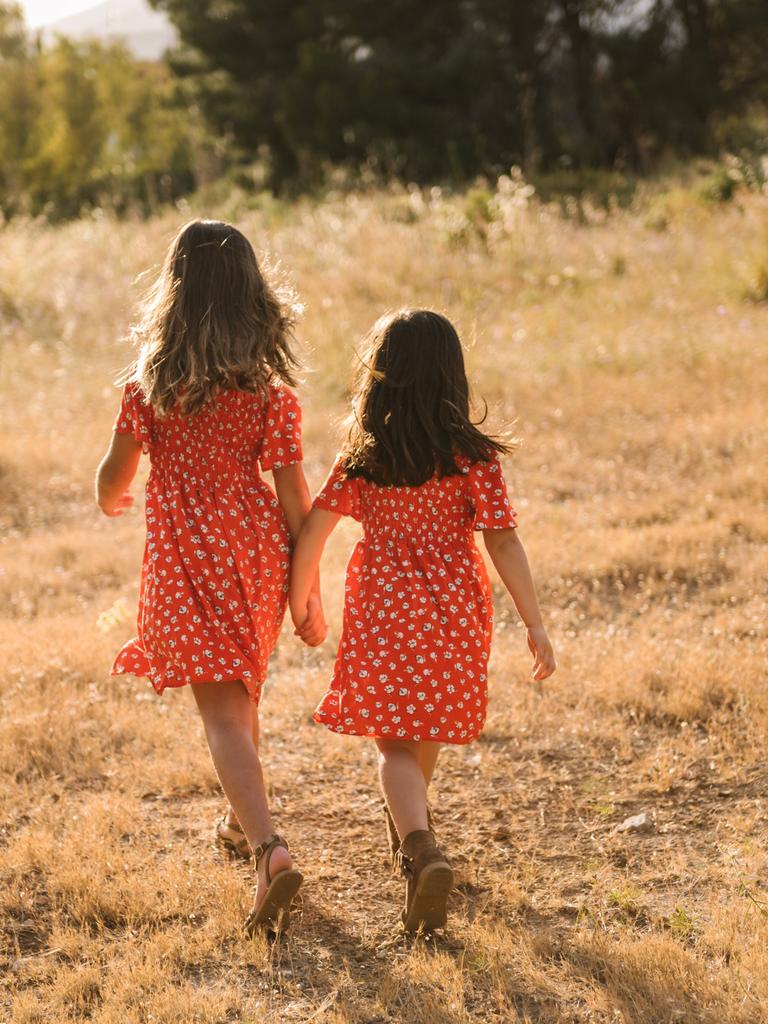 Zwei Schwester, die das gleiche Kleid tragen, gehen Hand in Hand durch die Natur.