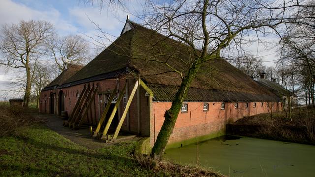 Zu sehen ist ein traditionelles Backsteinhaus in ländlicher Umgebung. Das Gebäude wird von mehreren schräg angebrachten Stützbalken stabilisiert, die an der Außenwand lehnen.