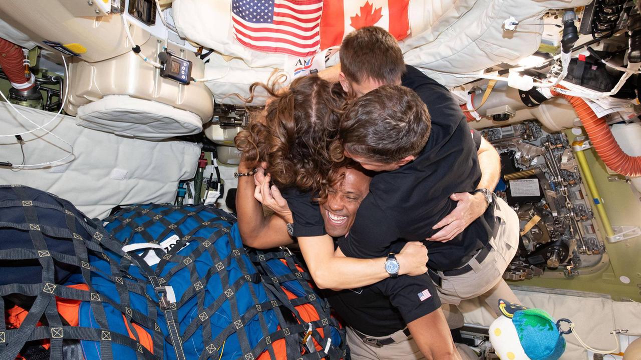 Die aus vier Leuten bestehende Crew der Artemis-2-Mission umarmt sich in ihrer Raumschiffkapsel, in der zahlreiche Ausrüstungsgegenstände gepackt sind Die aus vier Leuten bestehende Crew der Artemis-2-Mission umarmt sich in ihrer Raumschiffkapsel, in der zahlreiche Ausrüstungsgegenstände gepackt sind