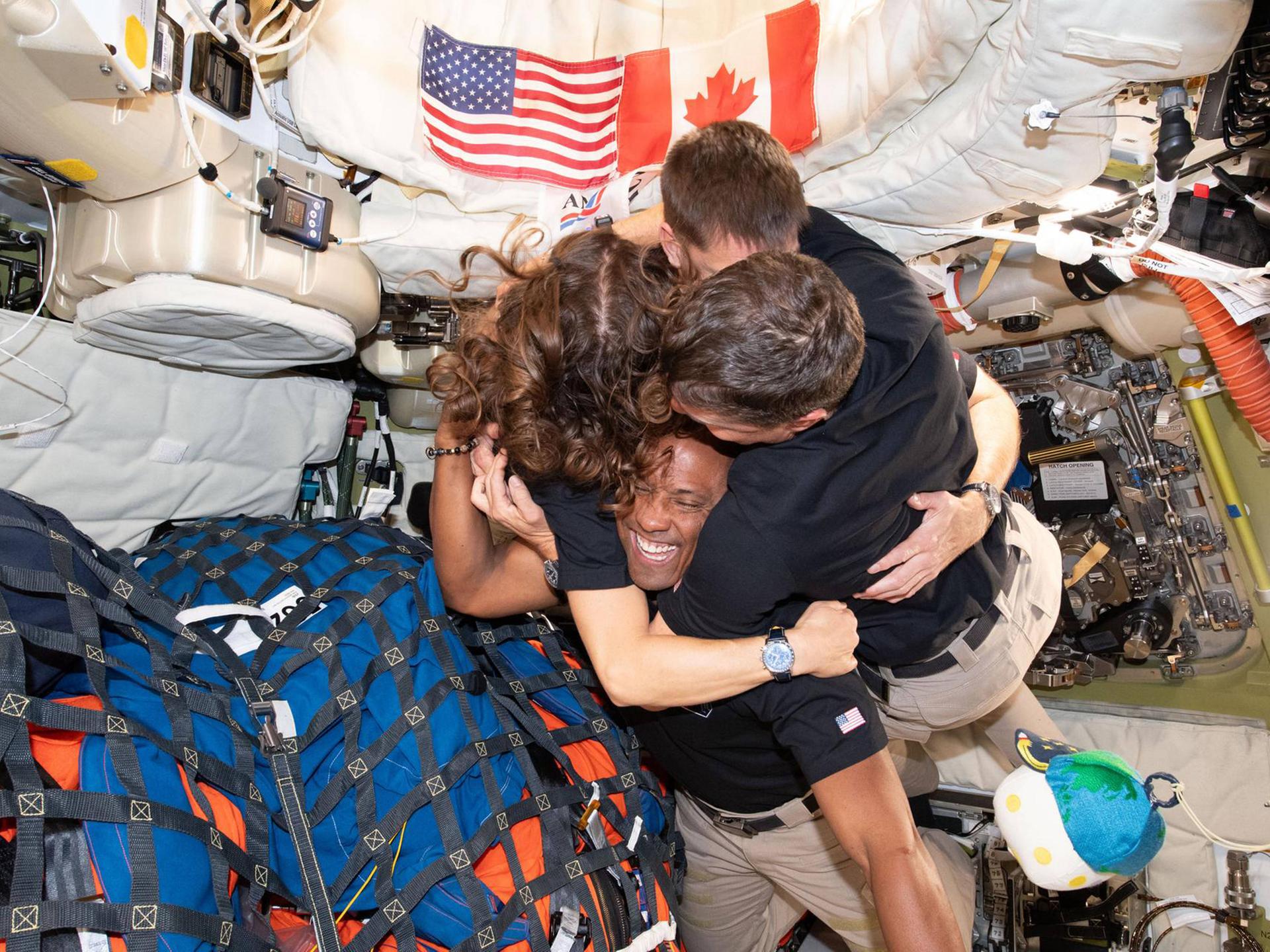 Die aus vier Leuten bestehende Crew der Artemis-2-Mission umarmt sich in ihrer Raumschiffkapsel, in der zahlreiche Ausrüstungsgegenstände gepackt sind