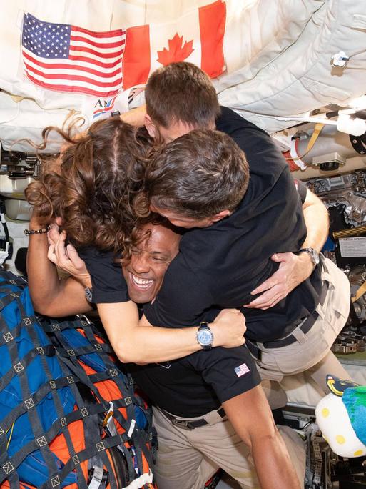 Die aus vier Leuten bestehende Crew der Artemis-2-Mission umarmt sich in ihrer Raumschiffkapsel, in der zahlreiche Ausrüstungsgegenstände gepackt sind