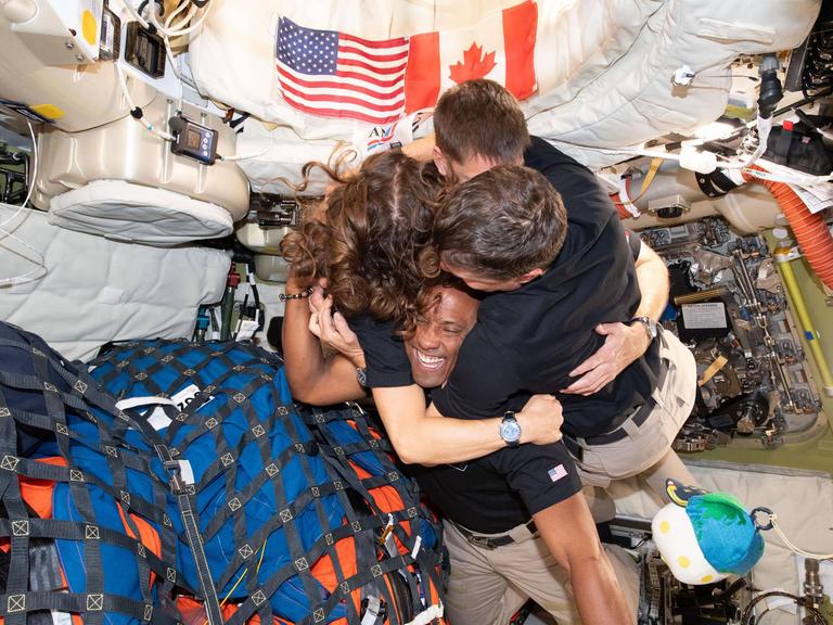 Die aus vier Leuten bestehende Crew der Artemis-2-Mission umarmt sich in ihrer Raumschiffkapsel, in der zahlreiche Ausrüstungsgegenstände gepackt sind