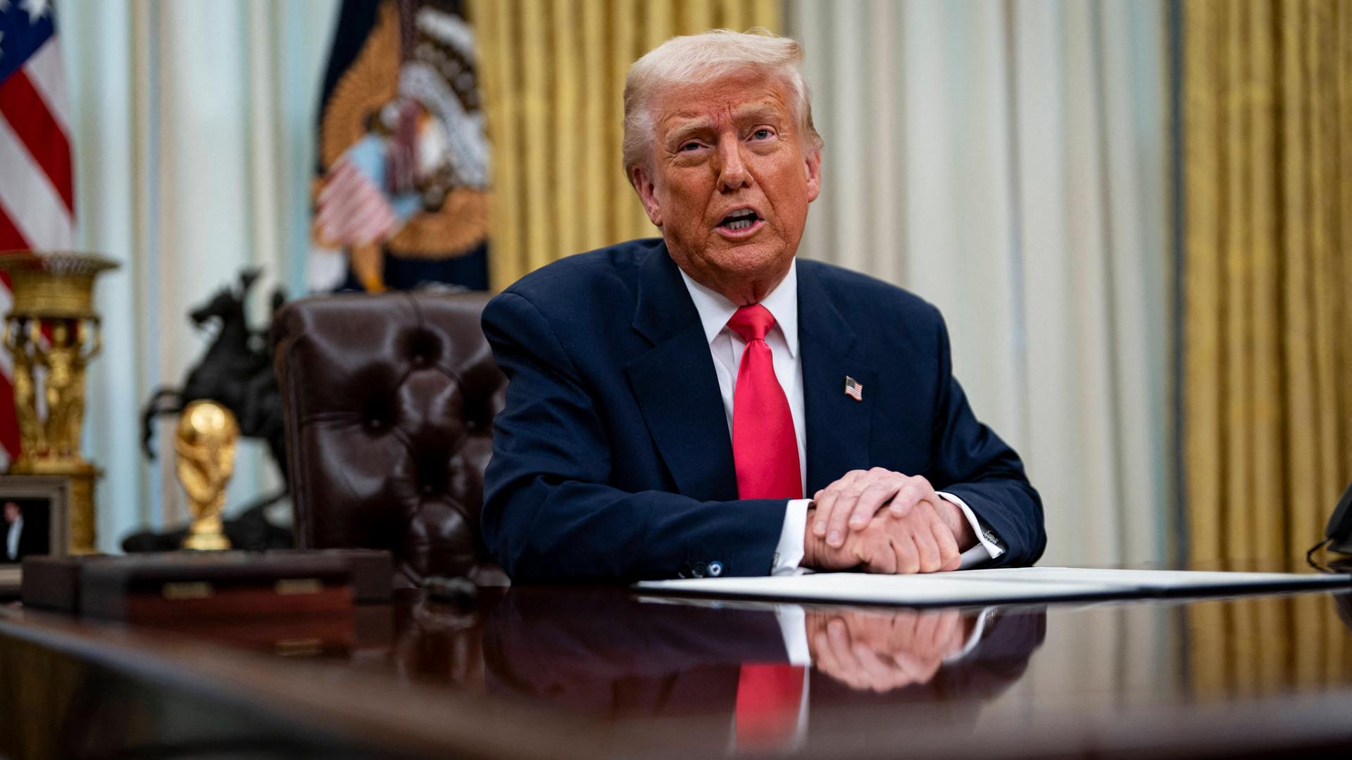 US-Präsident Donald Trump sitzt im Oval Office an seinem Schreibtisch. Vor ihm liegen Unterlagen, die er unterzeichnet hat. 