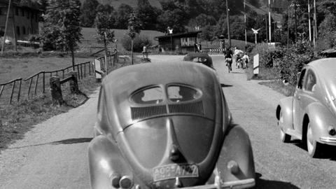 Das Hörspiel schildert Hugos Kampf mit seinem Kriegs- und Fluchtrauma in der Zeit des Wirtschaftswunders. Zu sehen: Eine Landstrasse bei München mit einem VW Käfer im Jahr 1953.