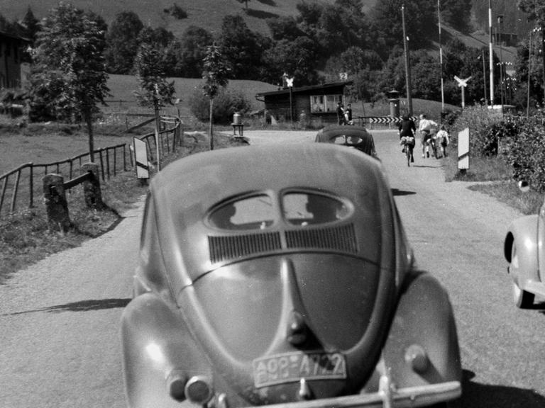 Das Hörspiel schildert Hugos Kampf mit seinem Kriegs- und Fluchtrauma in der Zeit des Wirtschaftswunders. Zu sehen: Eine Landstrasse bei München mit einem VW Käfer im Jahr 1953.